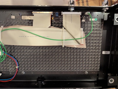 Focus on the back of a flipdot panel. There is a large number of solder joints for the dot matrix. One can also see that each panel has two 40-pin ribbon connectors and a single green wire running to them. On the panel PCB, there are only very few electronic components.